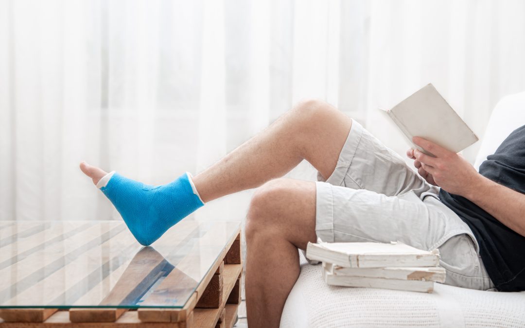 Man with a broken leg in a cast sits at home and reads books.